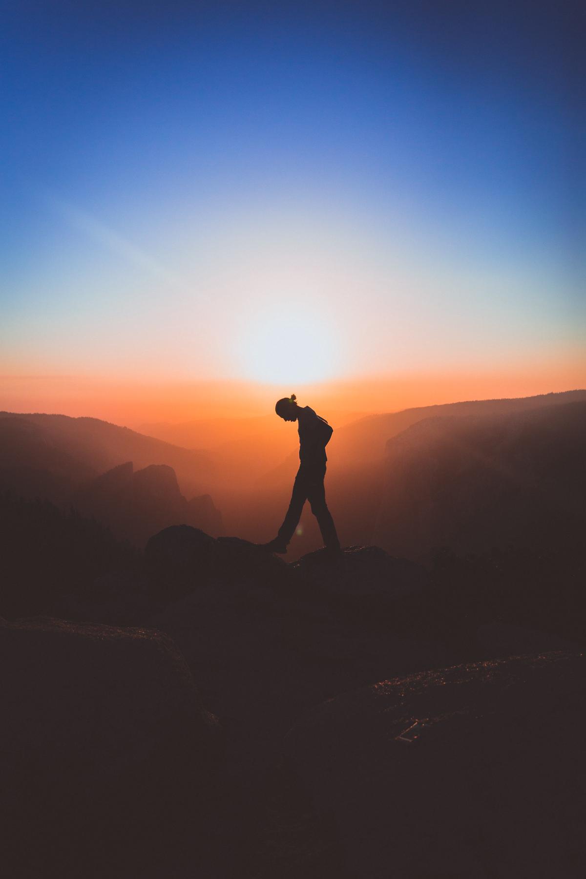 An image of a person standing on a mountain peak, looking out at the landscape before them. The image represents the idea of achieving goals through motivation and passion.